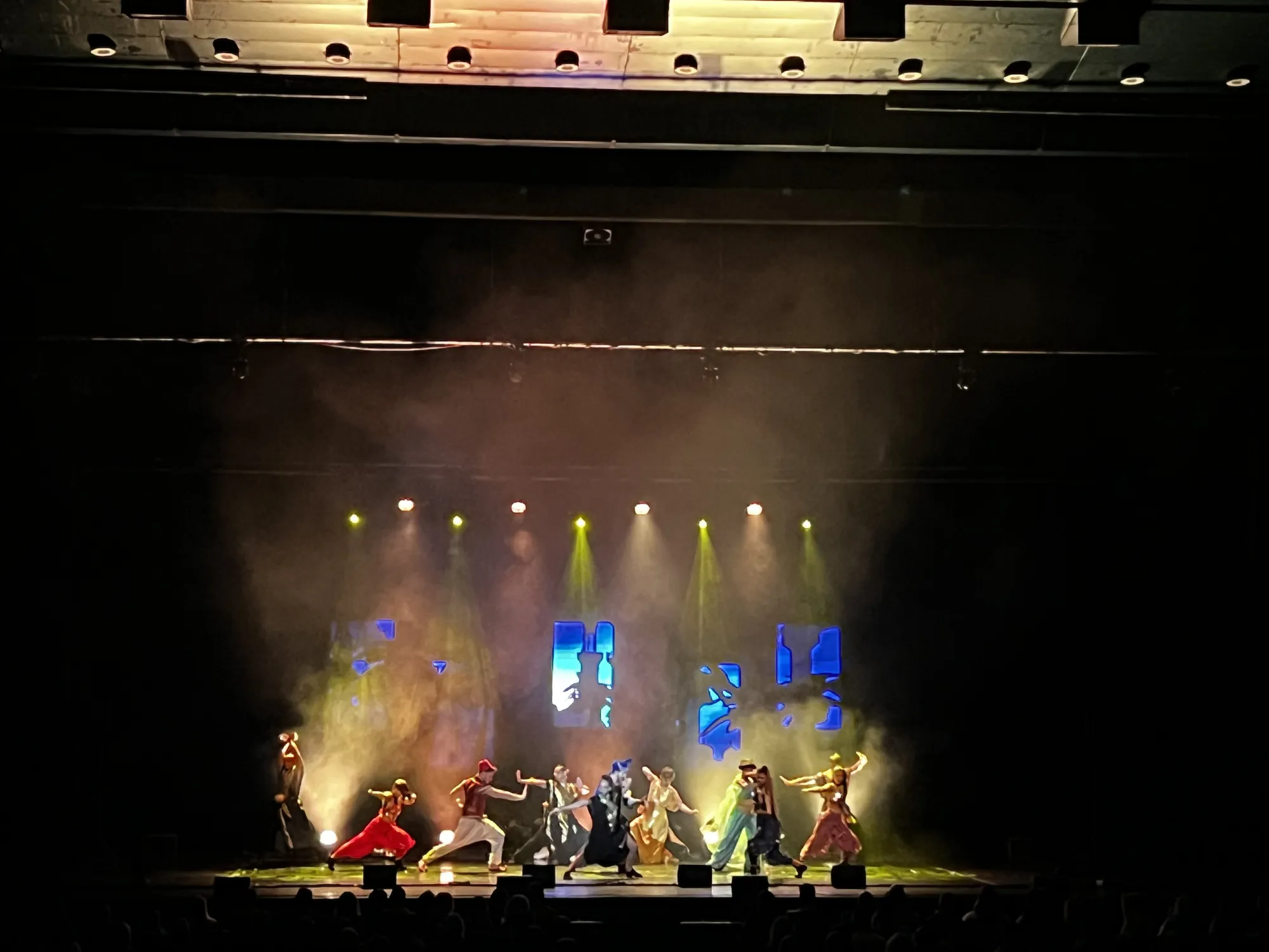 Жълти и зелени лъчи през хейз и дим пред LED екрани със сини графики